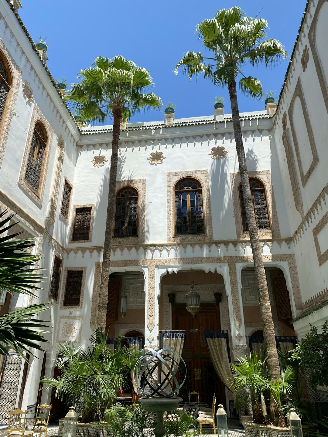 Palm trees stand in an opulent courtyard with carved white buildings.