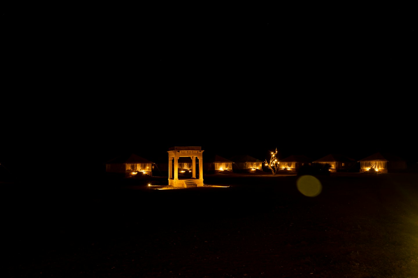 Illuminated luxury desert tents and a central stone gazebo at night.